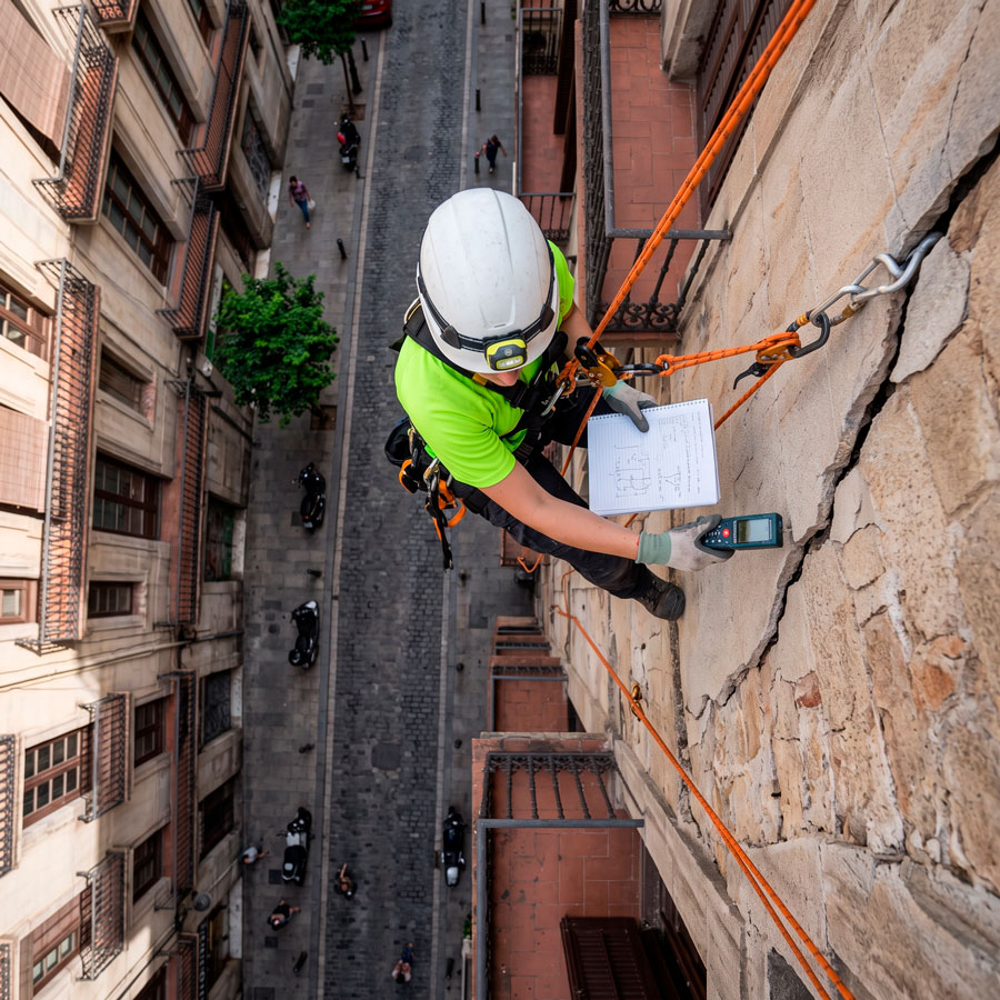 Persona-analizando-grieta-en-fachada-de-un-edificio-en-la-ciudad-de-barcelona Persona inspeccionando una grieta en la fachada de un edificio mediante técnicas de trabajos verticales