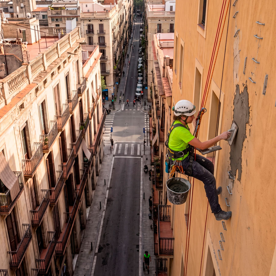 Saneado-de-fisuras-en-reparacion-de-grietas-en-fachadas-con-trabajos-verticales Técnico saneando una fisura en una reparación de grietas en fachadas con trabajos verticales
